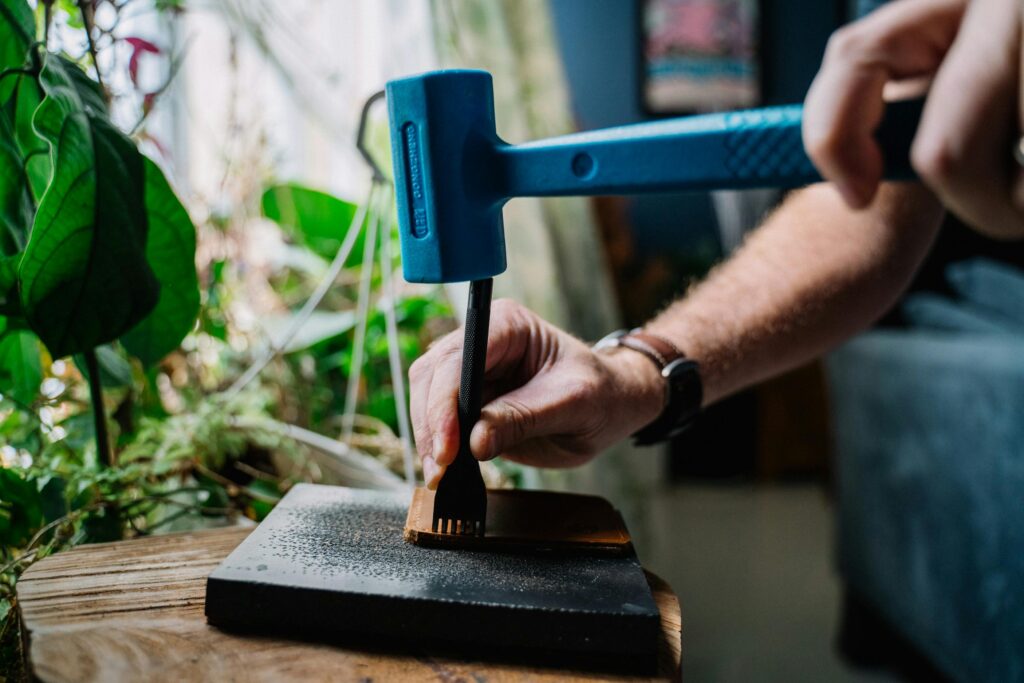 Hands skillfully hammering leather with tools in a studio setting surrounded by greenery.